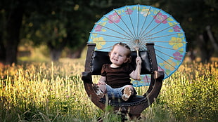 toddler wearing brown shirt and blue shorts holding blue oil paper umbrella sitting on black leather padded chair