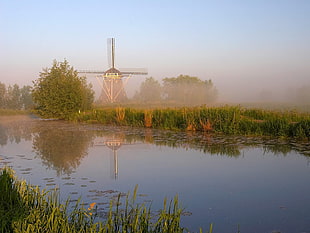 Wind mill near body of water surrounded with green grass