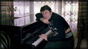man in black sweater sitting in front of black upright piano