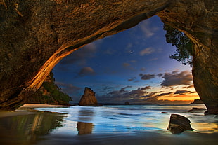 calm body of water under brown cave, cave, beach, sea, sunset