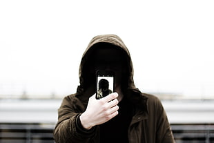 person wearing brown hoodie taking a Selfie during cloudy day