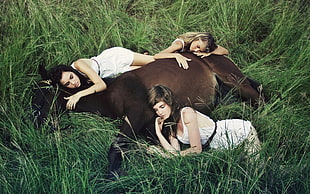 three women lying beside brown horse