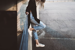 woman wearing black long-sleeved top and distressed blue jeans outfit leaning on gray metal railings