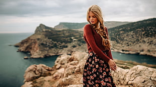 blonde haired woman in brown long-sleeve top standing on top of mountain beside body of water