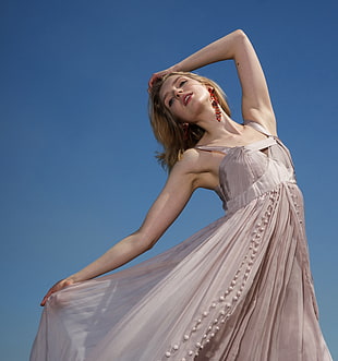 woman in grey sleeveless pleated dress holding her head under blue sky