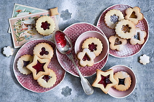 jam filled cookies served on white and red ceramic plates and bowls on grey wooden surface
