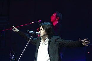 man in black jacket facing microphone on stage