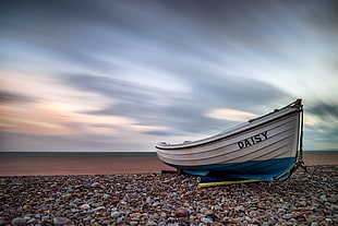 times lapsed photography of white and blue Daisy kaya boat on pebbles