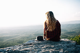 woman in red and black checked long-sleeved shirt sitting at the top of mountain during daytime HD wallpaper