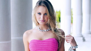 depth of field photo of woman wearing pink strapless sweetheart while holding her blonde hair
