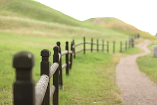 black wooden fence with road and green field during daytime
