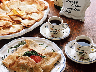 two cups of coffee served on saucers beside two plates of meal on brown wooden table