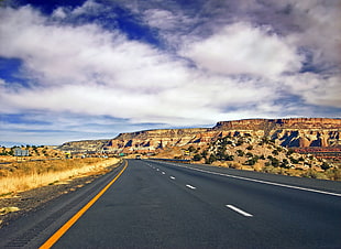 close up photo of gray road between brown valleys under blue sky