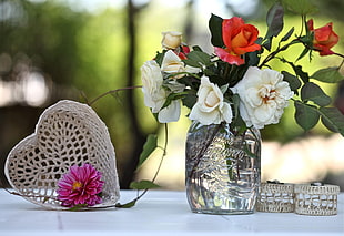 white-and-red flowers placed in glass jar next to heart-shaped white wicker box