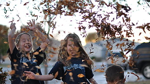 two girls wearing black crew-neck t-shirt playing dried leaves during daytime HD wallpaper