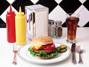 closeup photo of burger on white plate with spoon and bread knife and condiment shakers