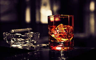 depth of field selective color photography of whiskey glass with ice and liquid beside tobacco on top of clear glass ashtray HD wallpaper