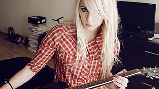 woman in red flannel dress shirt with blonde hair holding guitar