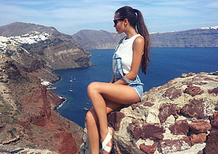 woman in white top sitting on rocky mountain at the seaside