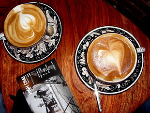 white-and-black ceramic mug with saucer set on brown wooden surface
