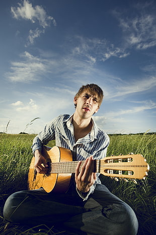 man sitting on grass playing guitar HD wallpaper