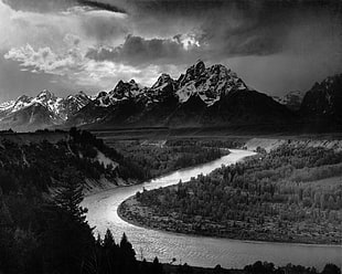 grayscale photography of body of water surrounded by trees with mountain range background
