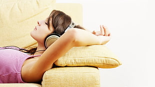 woman with gray headphones while lying on yellow pillow