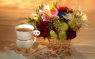 white ceramic teacup with tea besides artificial flowers