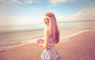blonde haired woman in purple and white floral dress in front of beach while laughing