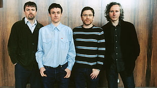four man standing near brown wooden wall in-front of the camera