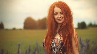 red-haired woman in brown, white, and black paisley strap-less top near green field during daytime