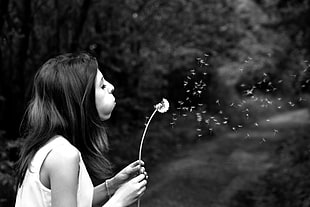 grayscale photo of woman blowing dandelion seeds