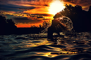 silhouette photo of woman in body body of water during sunset