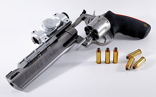 silver and black Raging Bull revolver gun and gold bullets