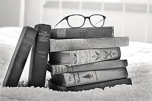 pile of books and eyeglasses on the top of it grayscale photo