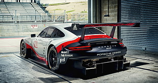 black, red, and white Porsche racing coupe park near gray metal roll down gate
