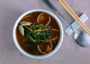 cooked soup with oysters in white bowl near stainless steel spoon and pair of chopsticks