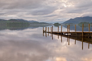 wooden dock reflecting over calm body of water with mountains at distance