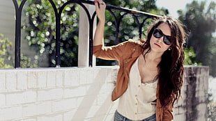woman in white spaghetti strap top and brown jacket near white concrete wall during daytime