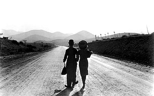 grayscale photo of man and woman walking through street