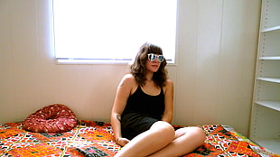 woman wearing black tank top and black shorts sitting on multicolored bed sheet