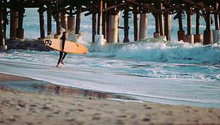 man wearing black wet suit and holding white snowboard going to the ocean