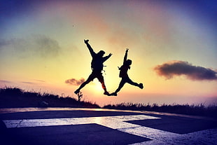 silhouette of two person jumping on helicopter dock during daytime HD wallpaper