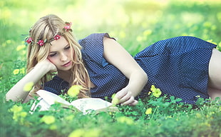 woman lying on green grass lawn reading book during daytime
