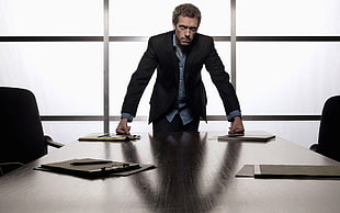 man wearing black suit standing with two fist on desk