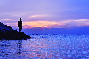 silhouette of person on rock near sea HD wallpaper