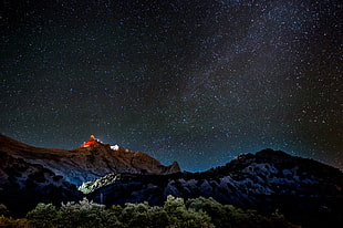 low angle photography of stars, mountains and green leafy trees