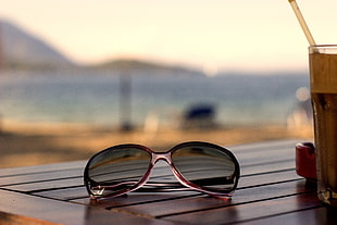 brown framed sunglasses near clear drinking glass