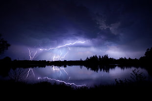 silhouette of body of water surrounded by trees with thunder