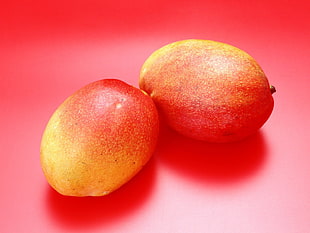 two oval red-and-yellow fruits on red surface